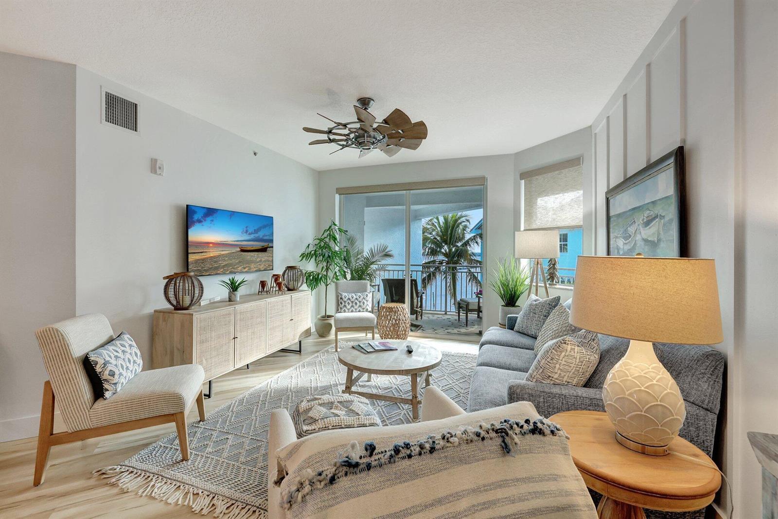 A bright living room features a gray sofa, patterned area rug, and balcony with palm trees — 875 NW Flagler Avenue # 404, Stuart FL 34994, STUART, FL