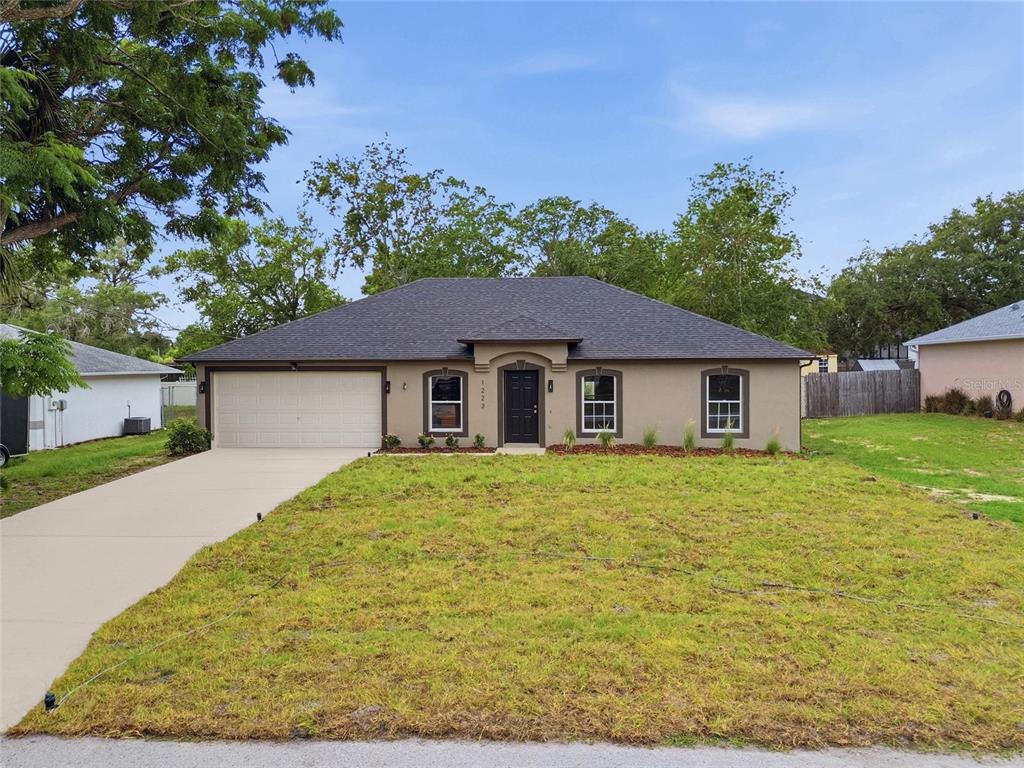 A single-story house with a beige stucco exterior, dark roof, and a front-facing garage — 1223 GATEWOOD AVENUE, SPRING HILL, FL
