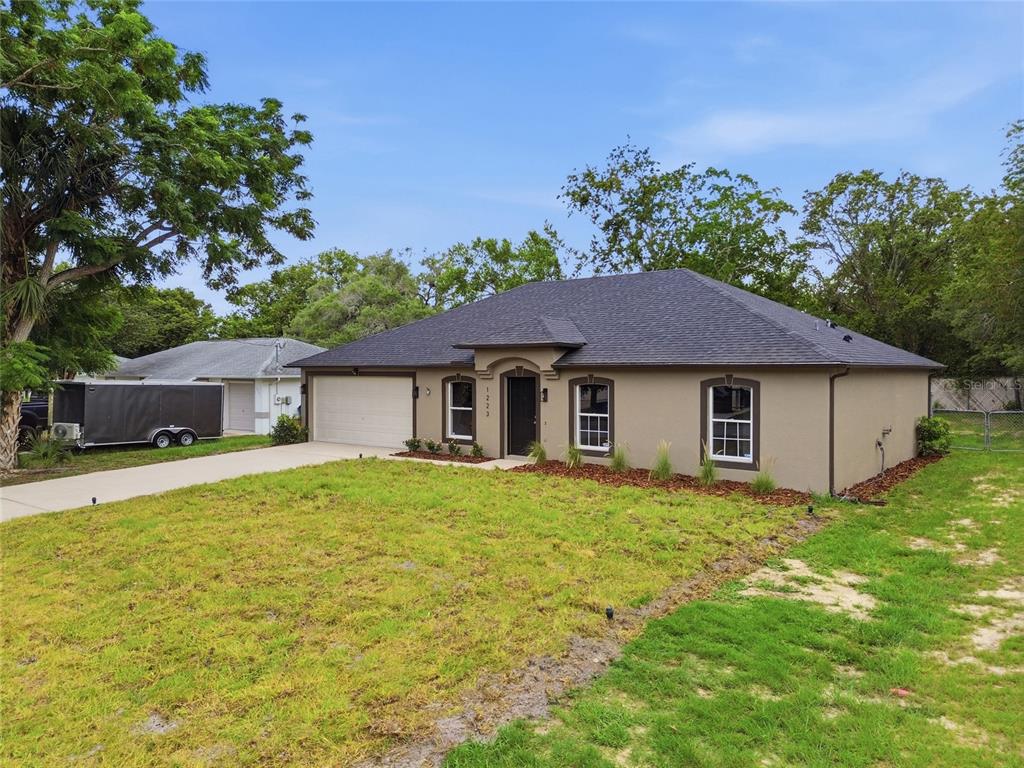 A single-story house with a tan exterior, dark roof, and attached garage sits on grass — 1223 GATEWOOD AVENUE, SPRING HILL, FL
