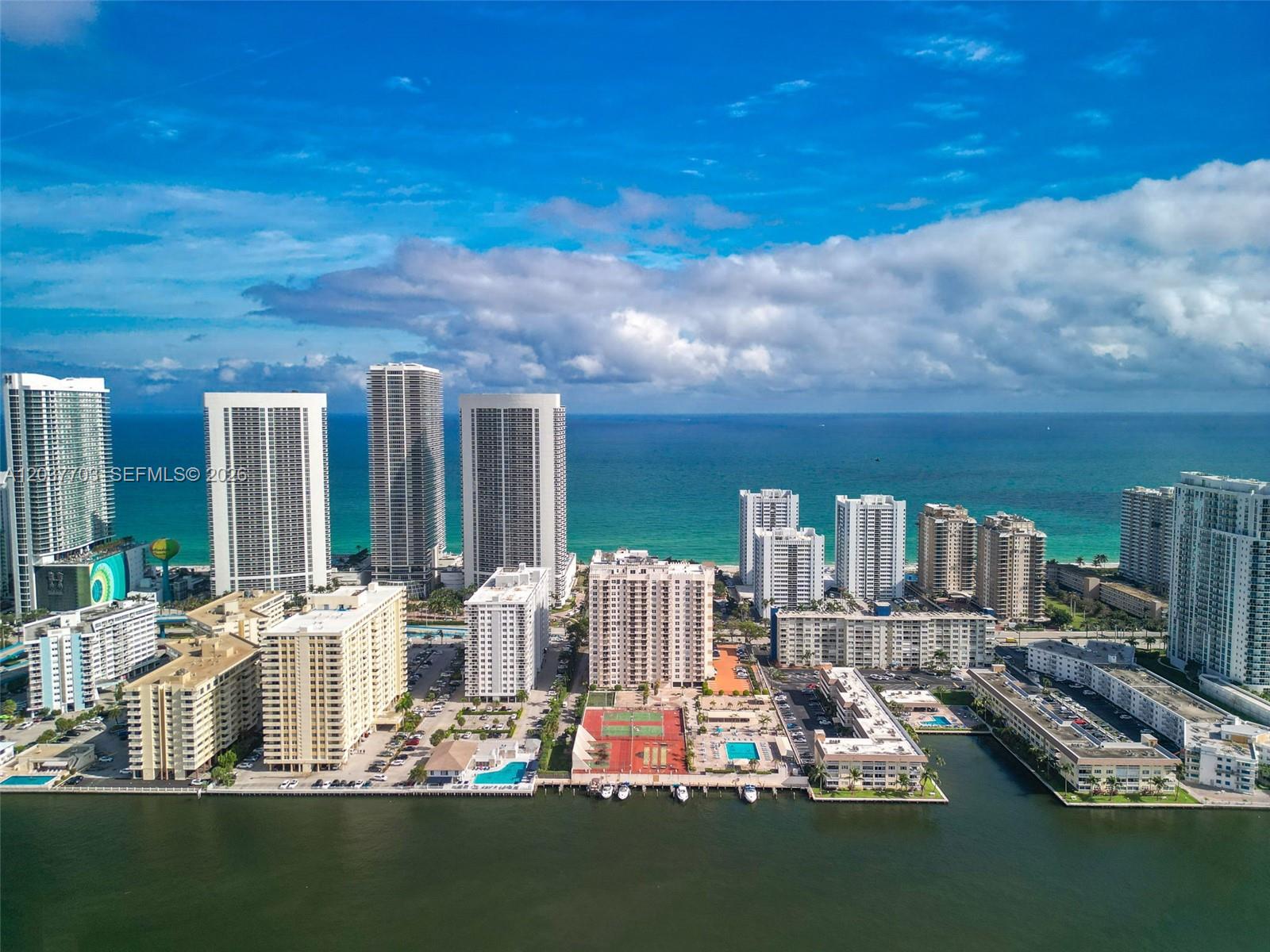 An aerial view shows high-rise residential buildings along a coastline with a bay in front — 1865 S Ocean Dr # 16B, Hallandale Beach FL 33009, HALLANDALE BEACH, FL