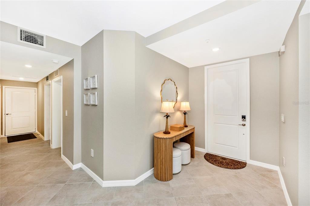 An entryway features a console table, two lamps, a mirror, and tiled flooring — 12685 RADIANCE COURT UNIT 101, VENICE, FL