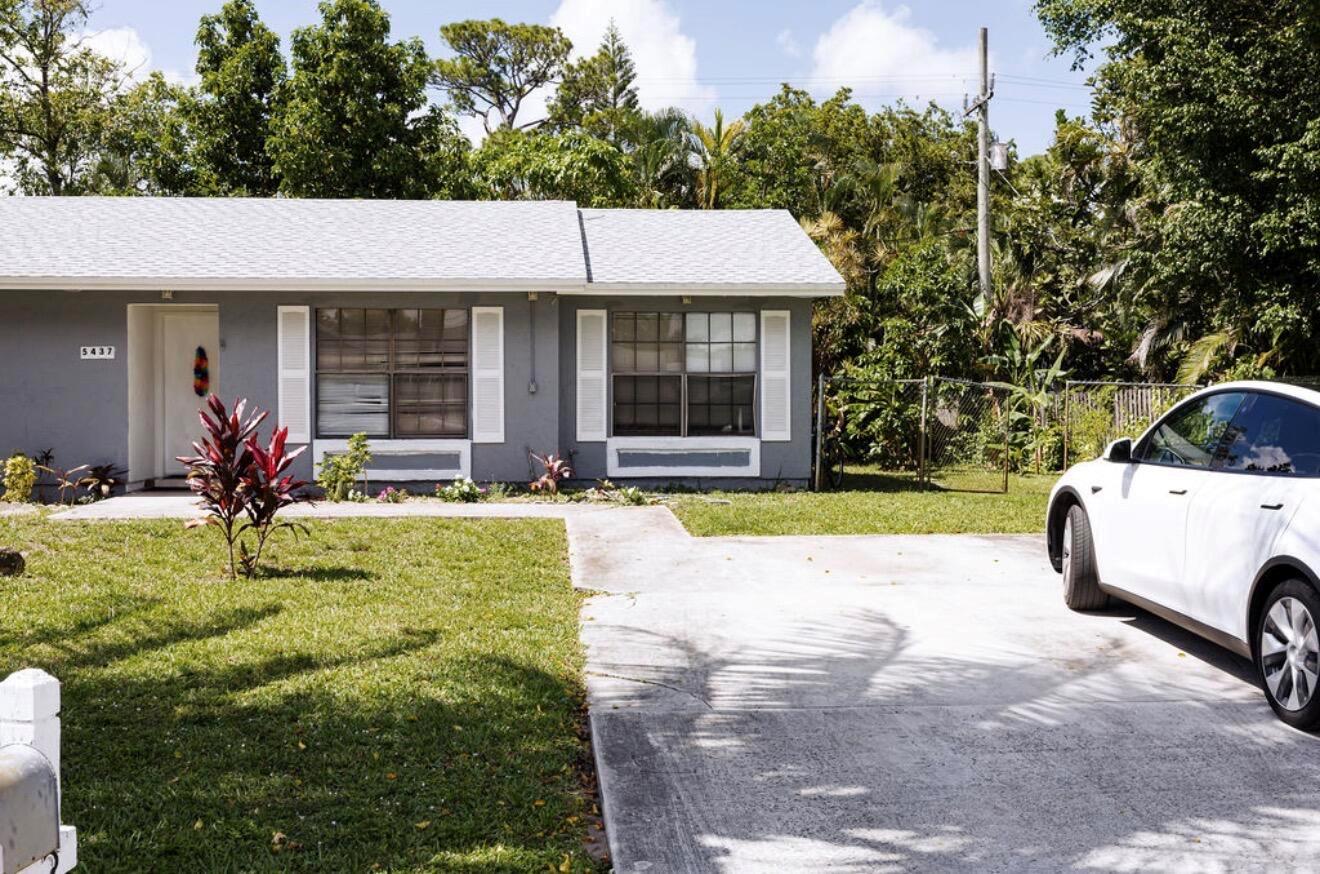 A gray single-story house with white shutters and a driveway sits behind a front lawn — 5437 Greenwood Drive, Delray Beach FL 33484, DELRAY BEACH, FL