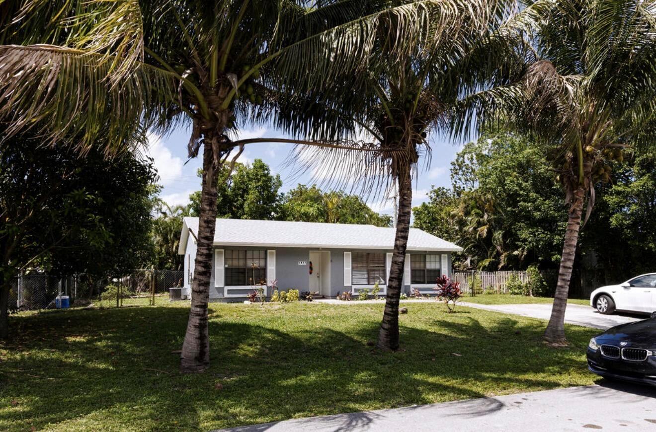 A single-story gray house with white shutters sits behind two palm trees on a lawn — 5437 Greenwood Drive, Delray Beach FL 33484, DELRAY BEACH, FL
