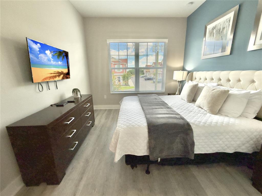 A bedroom features a king bed, a dark wood dresser, and a wall-mounted television — 7569 SUNNY DREAMS LANE, KISSIMMEE, FL