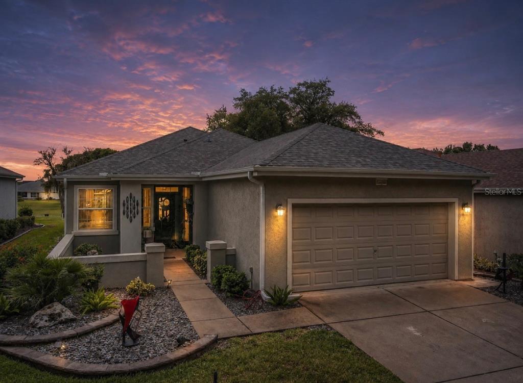 A single-story house with a two-car garage and a landscaped front yard at sunset — 13260 SE 92ND COURT ROAD, SUMMERFIELD, FL