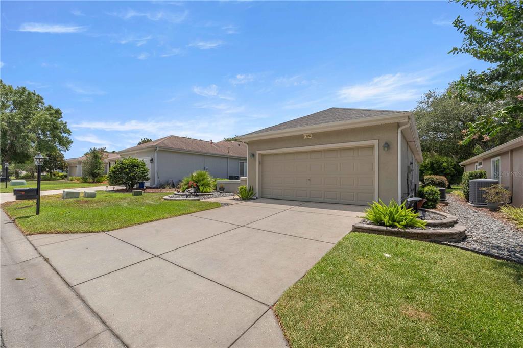 A suburban house features a concrete driveway leading to a two-car garage under a blue sky — 13260 SE 92ND COURT ROAD, SUMMERFIELD, FL