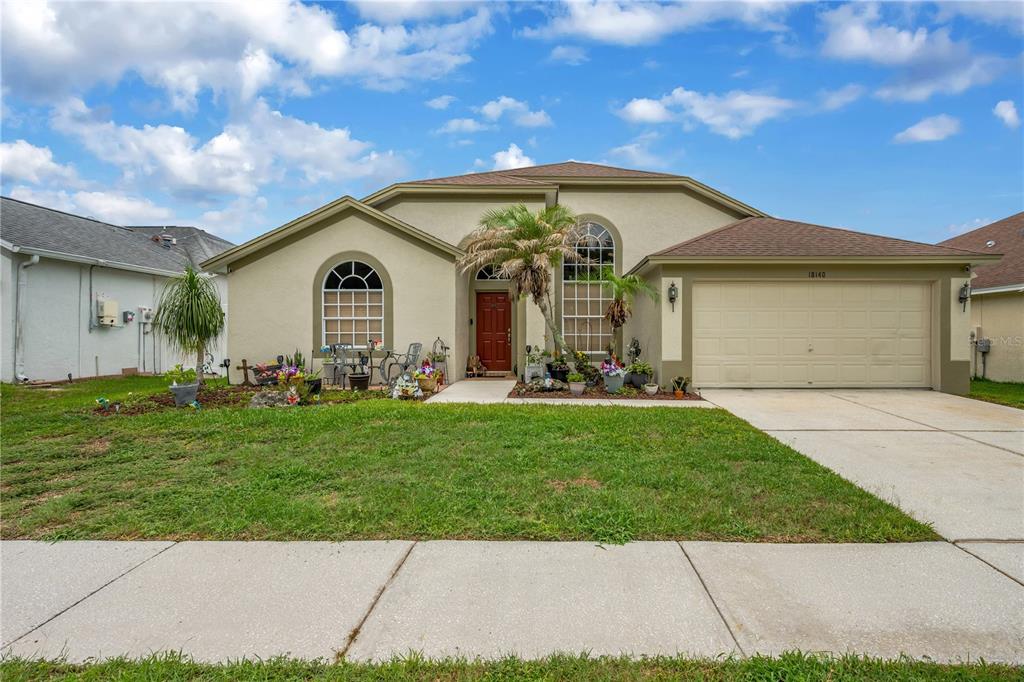 A single-story house with a beige stucco exterior, a red front door, and a two-car garage — 18140 PALM BREEZE DRIVE, TAMPA, FL