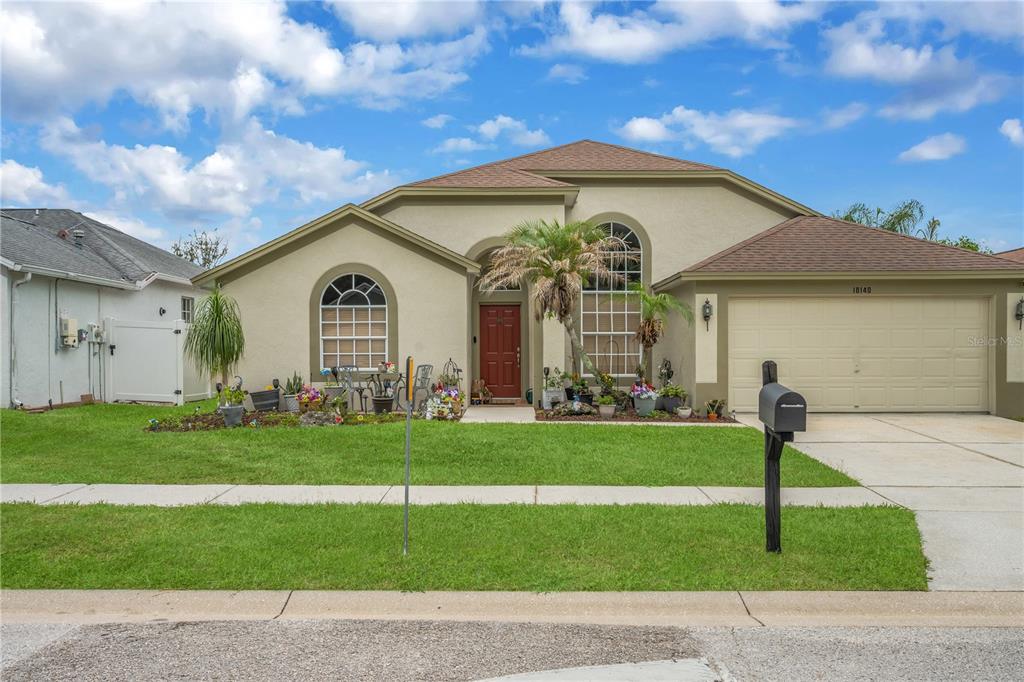 A single-story house with a tan stucco exterior, a two-car garage, and a red door — 18140 PALM BREEZE DRIVE, TAMPA, FL