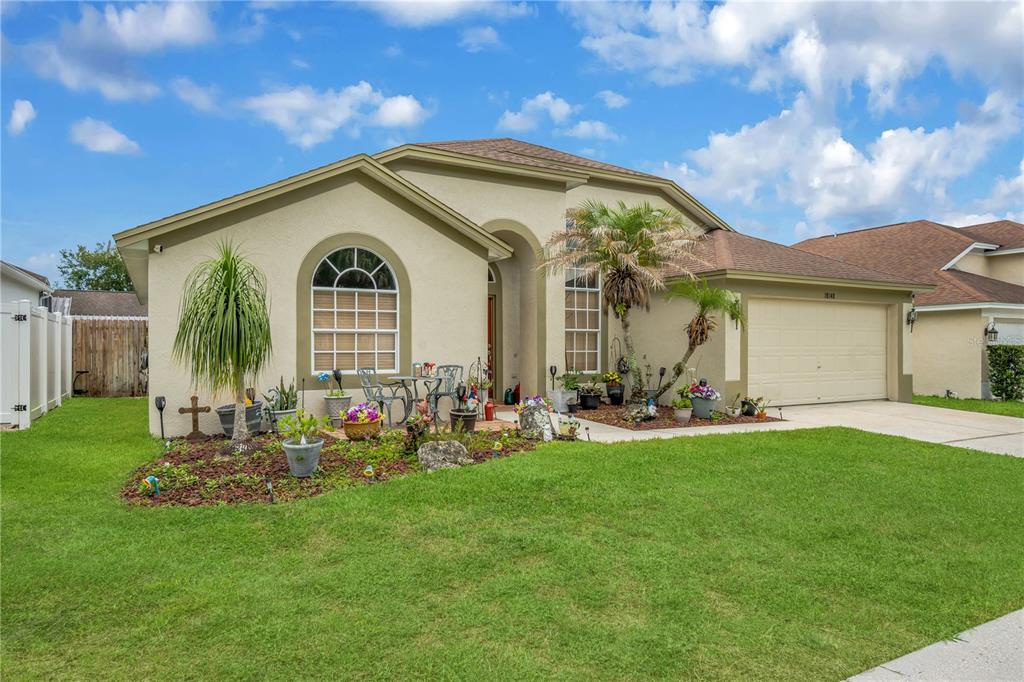 A single-story house with a beige stucco exterior, a two-car garage, and a front lawn — 18140 PALM BREEZE DRIVE, TAMPA, FL