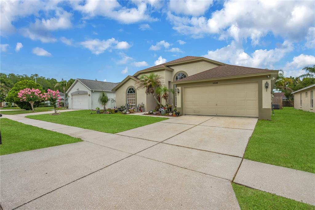 A tan single-story house with a two-car garage and a concrete driveway under a blue sky — 18140 PALM BREEZE DRIVE, TAMPA, FL