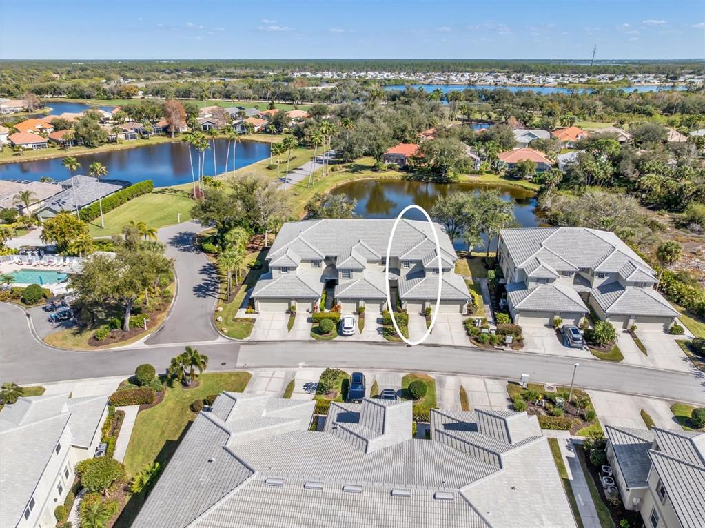 An aerial view shows multi-unit residential buildings with gray tiled roofs near a pond — 3322 GRAND VISTA COURT UNIT 203, PORT CHARLOTTE, FL