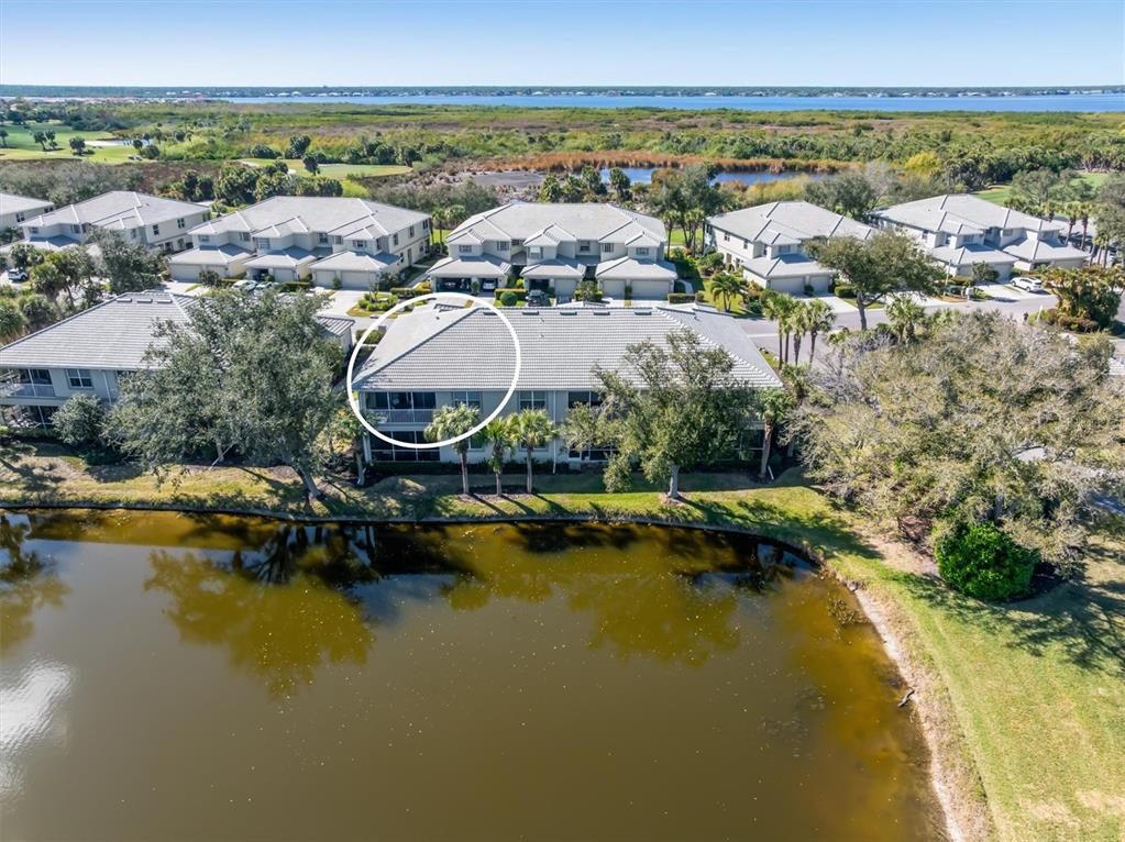 An aerial view shows a multi-story residential building with a tiled roof beside a pond — 3322 GRAND VISTA COURT UNIT 203, PORT CHARLOTTE, FL