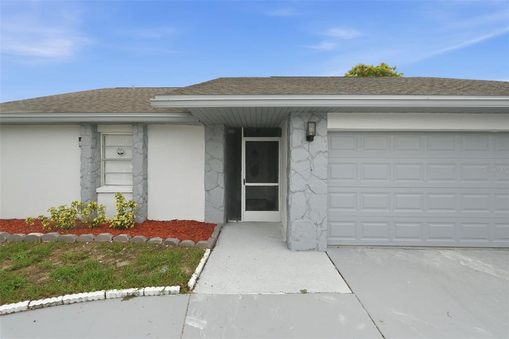 A single-story house exterior features a gray garage door, stone accents, and a front entryway — 11320 PARTRIDGE DRIVE, TAMPA, FL