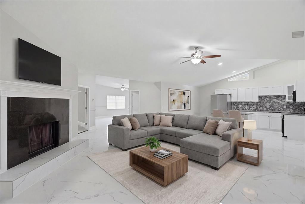 An open-concept living room features a grey sectional sofa, fireplace, and white marble flooring — 11320 PARTRIDGE DRIVE, TAMPA, FL