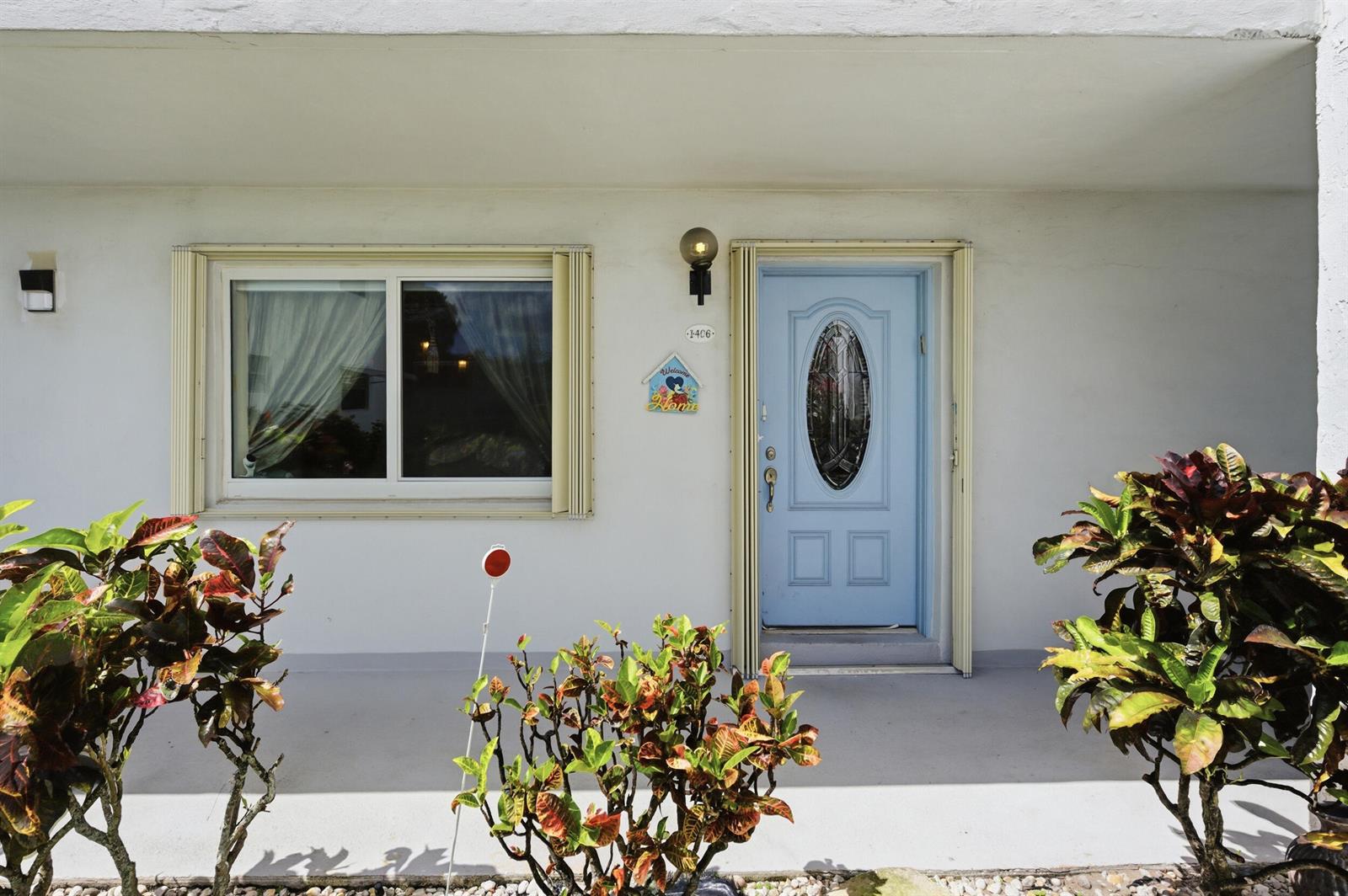 A light blue front door with an oval window sits beside a window on a porch — 406 Saxony I, Delray Beach FL 33446, DELRAY BEACH, FL