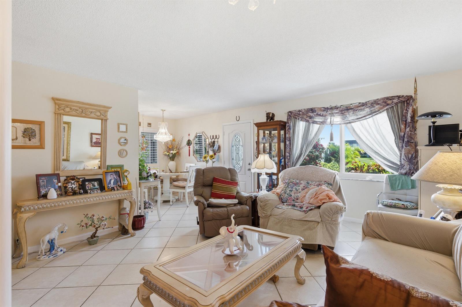 A living room with tile flooring, a coffee table, armchairs, and an adjacent dining area — 406 Saxony I, Delray Beach FL 33446, DELRAY BEACH, FL