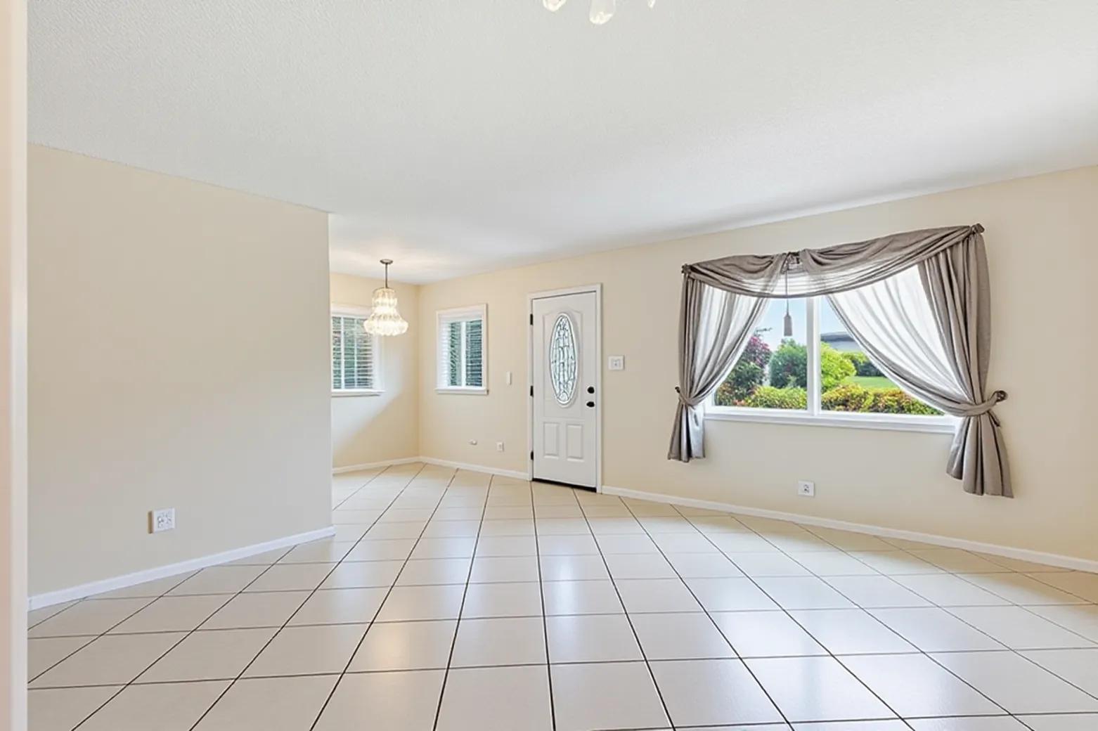 An empty room with beige walls, tile flooring, a front door, and a large window — 406 Saxony I, Delray Beach FL 33446, DELRAY BEACH, FL