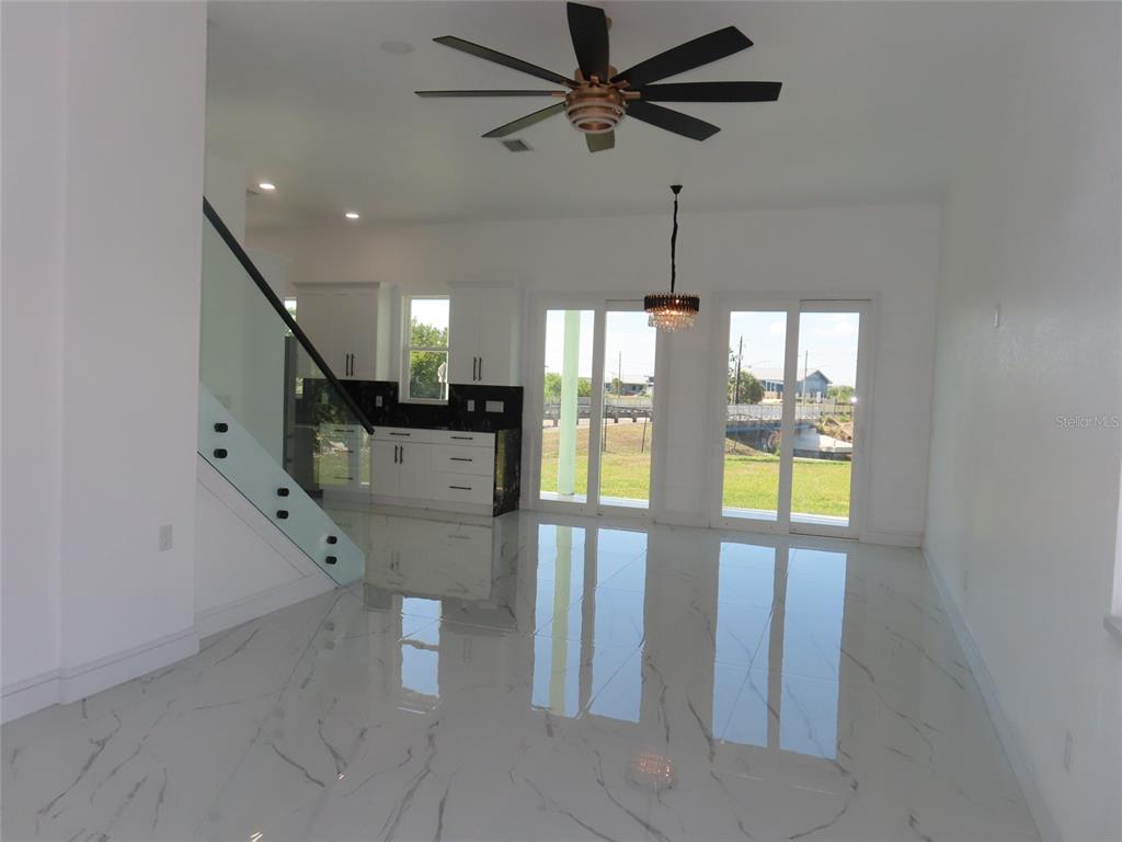 An open-concept living area features white marble-look tile floors, a glass-railed staircase, and sliding doors — 6510 SIMONE SHORES CIR, APOLLO BEACH, FL