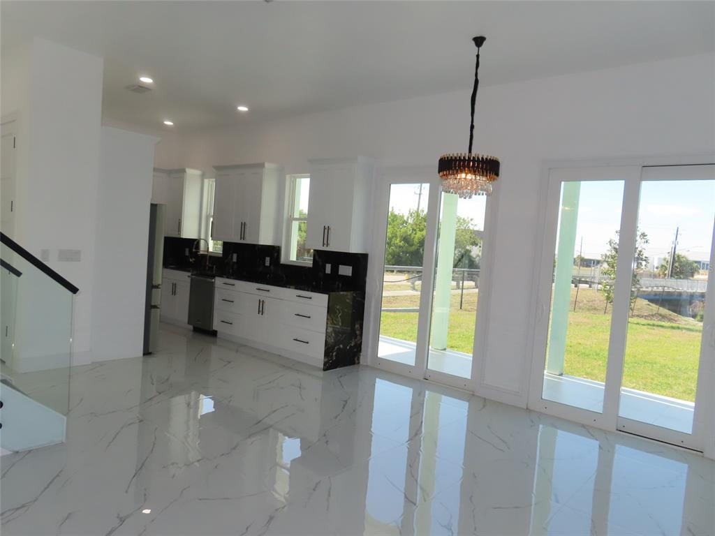 A modern kitchen with white cabinets, black countertops, and marble-look tile flooring opens to outdoors — 6510 SIMONE SHORES CIR, APOLLO BEACH, FL