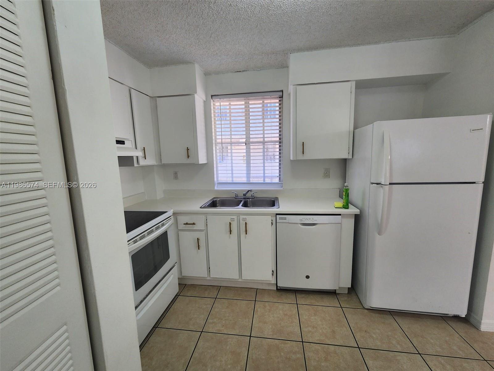 A kitchen features white cabinets, white appliances, a double sink, and light-colored tile flooring — 6195 NW 186th St # 309, Hialeah FL 33015, HIALEAH, FL