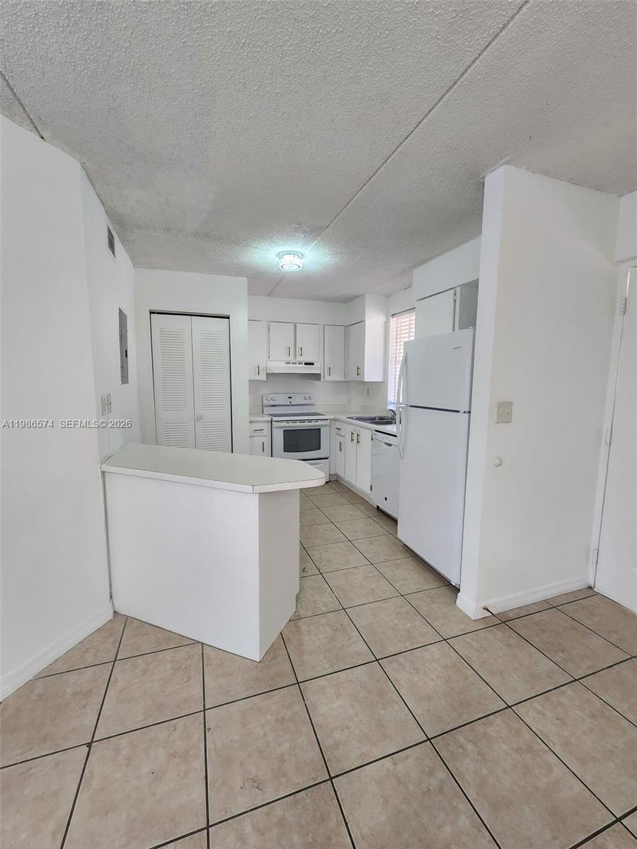 A white kitchen features tile flooring, white cabinetry, and a breakfast bar — 6195 NW 186th St # 309, Hialeah FL 33015, HIALEAH, FL