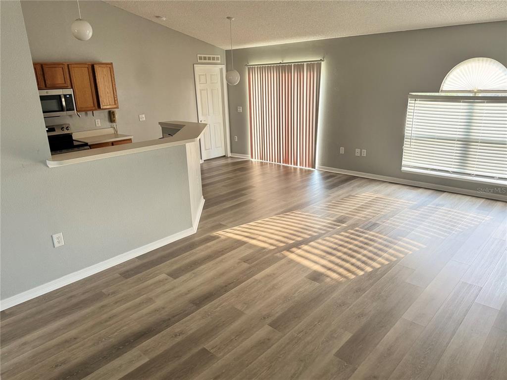 An open-concept living area features wood-look flooring, a kitchen pass-through, and sliding glass doors — 3080 UTAH DRIVE, DELTONA, FL
