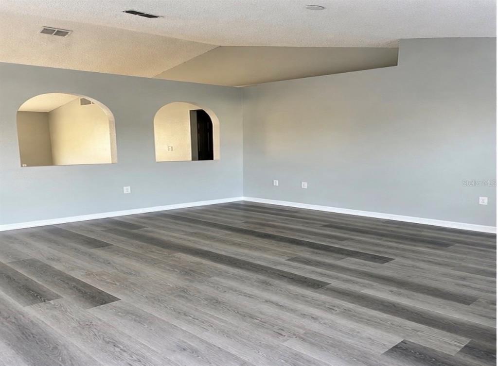 An empty room features gray walls, arched cutouts, and wood-look vinyl plank flooring — 3080 UTAH DRIVE, DELTONA, FL