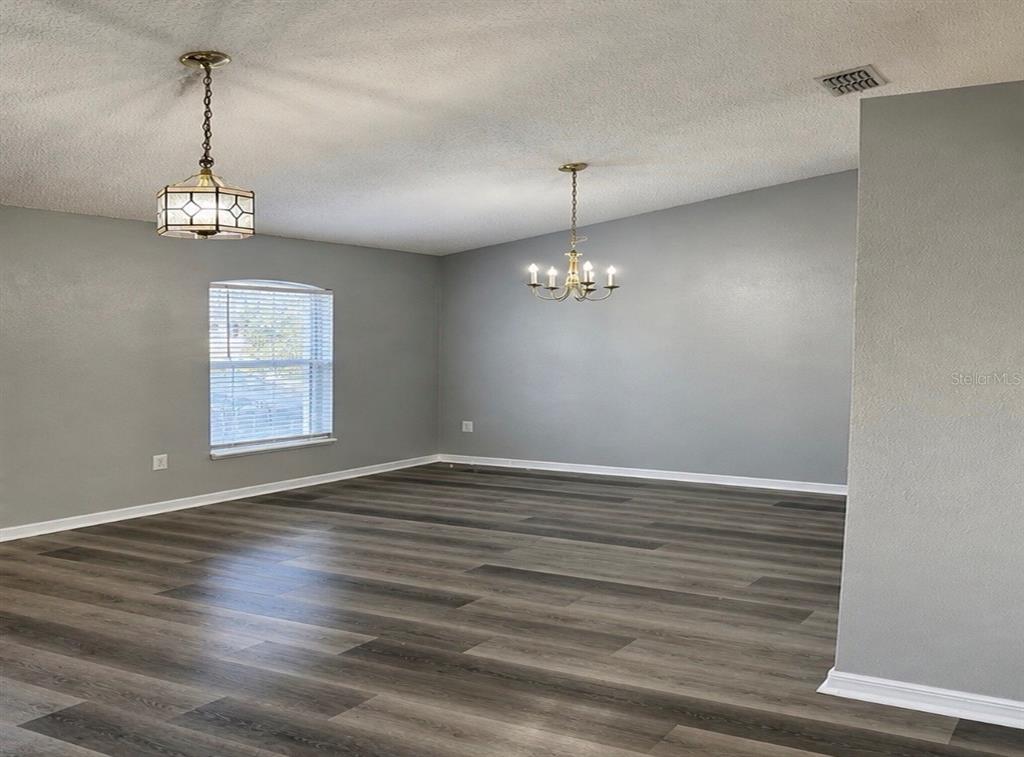 An empty room features gray walls, wood-look flooring, and two distinct hanging light fixtures — 3080 UTAH DRIVE, DELTONA, FL