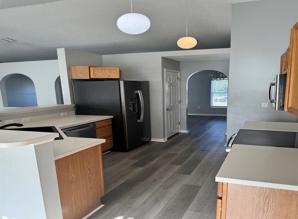 A kitchen with wood cabinets, light countertops, and grey wood-look flooring leads to an archway — 3080 UTAH DRIVE, DELTONA, FL