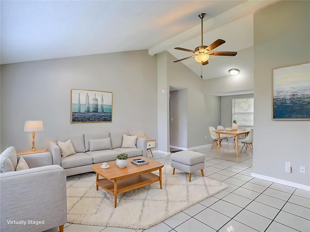 A living room with a vaulted ceiling, light gray walls, tile floors, and neutral furniture — 6701 VILLAGE GROVE COURT, TAMPA, FL