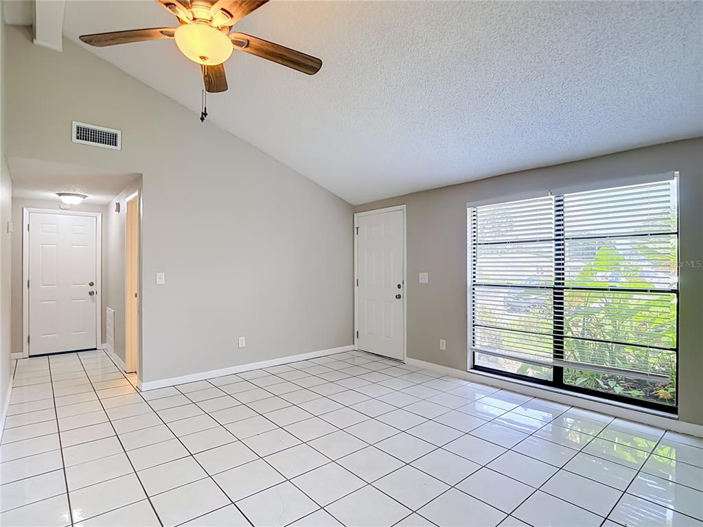 An empty room with white tile flooring, a vaulted ceiling, and a ceiling fan — 6701 VILLAGE GROVE COURT, TAMPA, FL