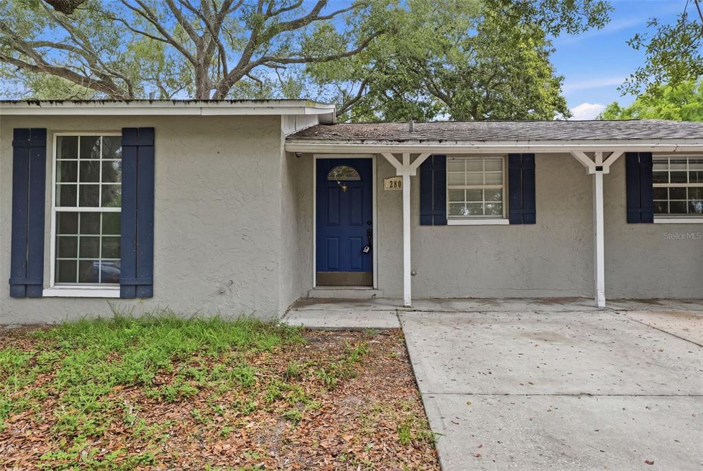 A single-story house exterior features a blue front door, dark shutters, and a concrete driveway — 2804 APPLEWOOD DRIVE, CLEARWATER, FL
