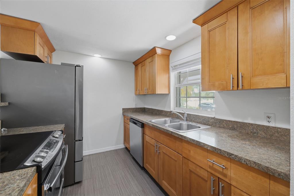 A kitchen features light wood cabinets, granite countertops, stainless steel appliances, and gray wood-look flooring — 2804 APPLEWOOD DRIVE, CLEARWATER, FL