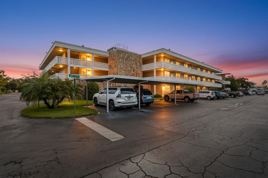 A three-story apartment building with a stone facade and a covered parking area at sunset — 5095 BAY STREET NE UNIT 210, ST PETERSBURG, FL