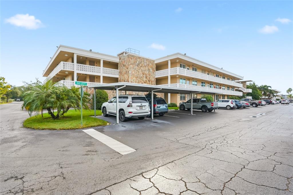 A multi-story apartment building features a covered parking area with several parked vehicles — 5095 BAY STREET NE UNIT 210, ST PETERSBURG, FL