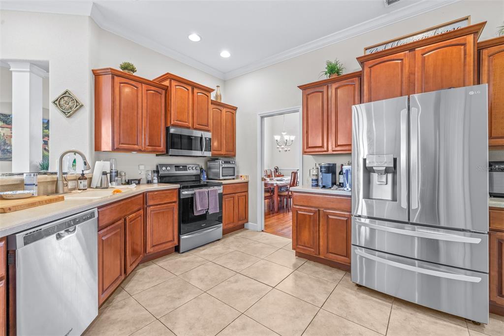 A kitchen features wood cabinets, stainless steel appliances, tile flooring, and a view into a dining room — 6798 HARTSWORTH DRIVE, LAKELAND, FL