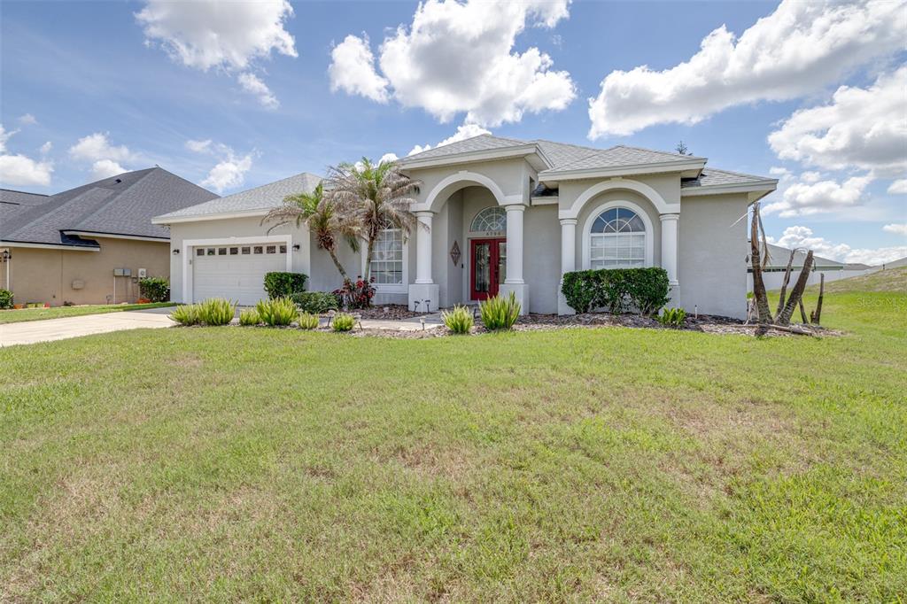 A single-story house with a beige stucco exterior, a red front door, and a garage — 6798 HARTSWORTH DRIVE, LAKELAND, FL
