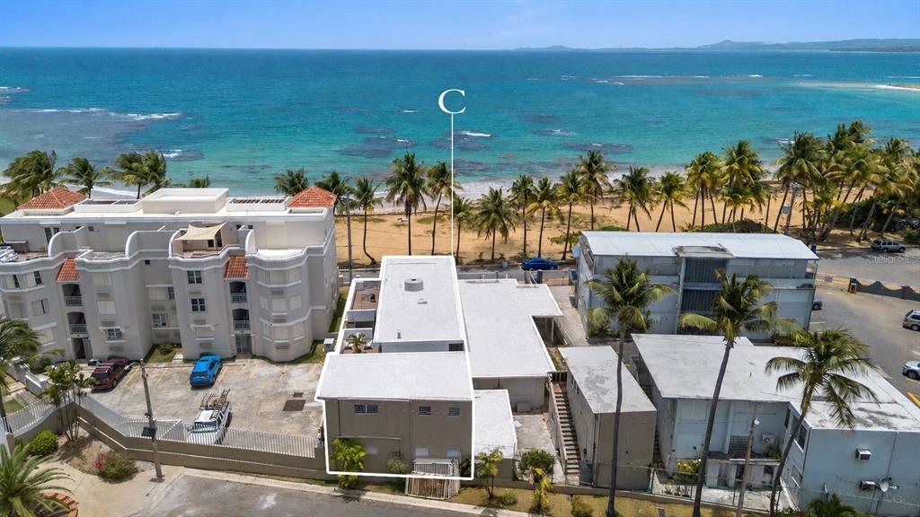 An aerial view shows a multi-story building complex situated directly on a sandy beach — Luquillo BEACH UNIT A-25, LUQUILLO, PR