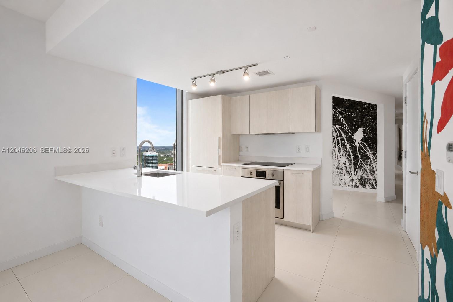 A modern kitchen features white countertops, light wood cabinetry, and a view of the city — 501 NE 31st St # 3208, Miami FL 33137, MIAMI, FL