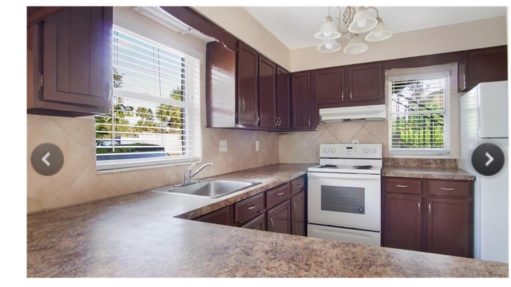 A kitchen with dark wood cabinets, laminate countertops, a white stove, and two windows — 6010 AMBERLY AVENUE UNIT F, ORLANDO, FL