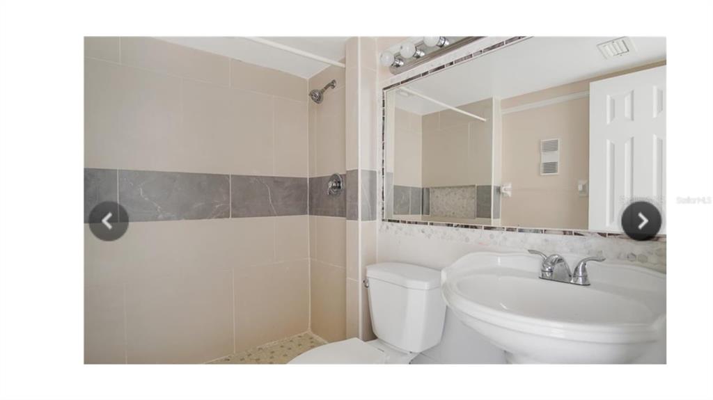 A bathroom features a tiled shower, a white pedestal sink, and a large wall mirror — 6010 AMBERLY AVENUE UNIT F, ORLANDO, FL