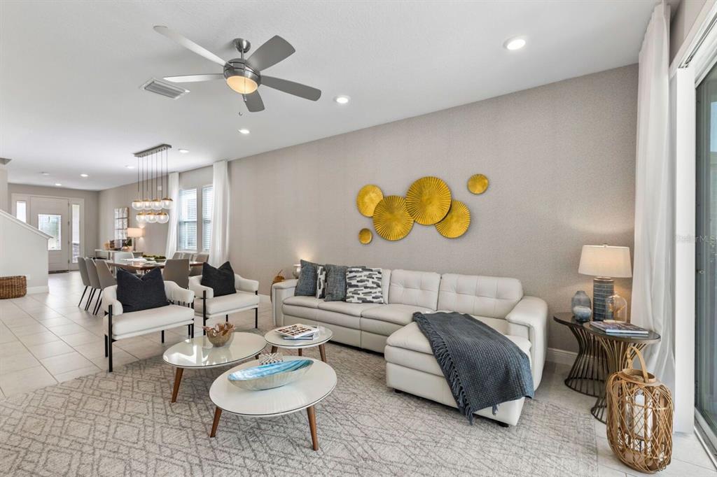 A living room with a white sectional, two armchairs, glass coffee tables, and gold wall art — 353 SOUTHFIELD STREET, KISSIMMEE, FL