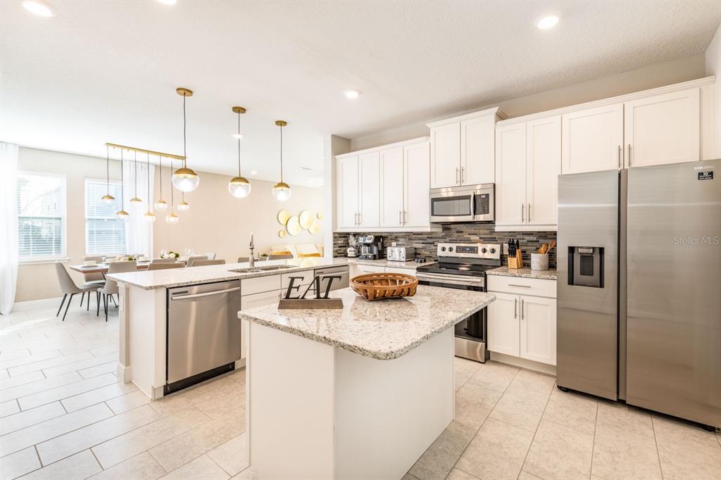 A modern kitchen features white cabinets, granite countertops, stainless steel appliances, and a central island — 353 SOUTHFIELD STREET, KISSIMMEE, FL