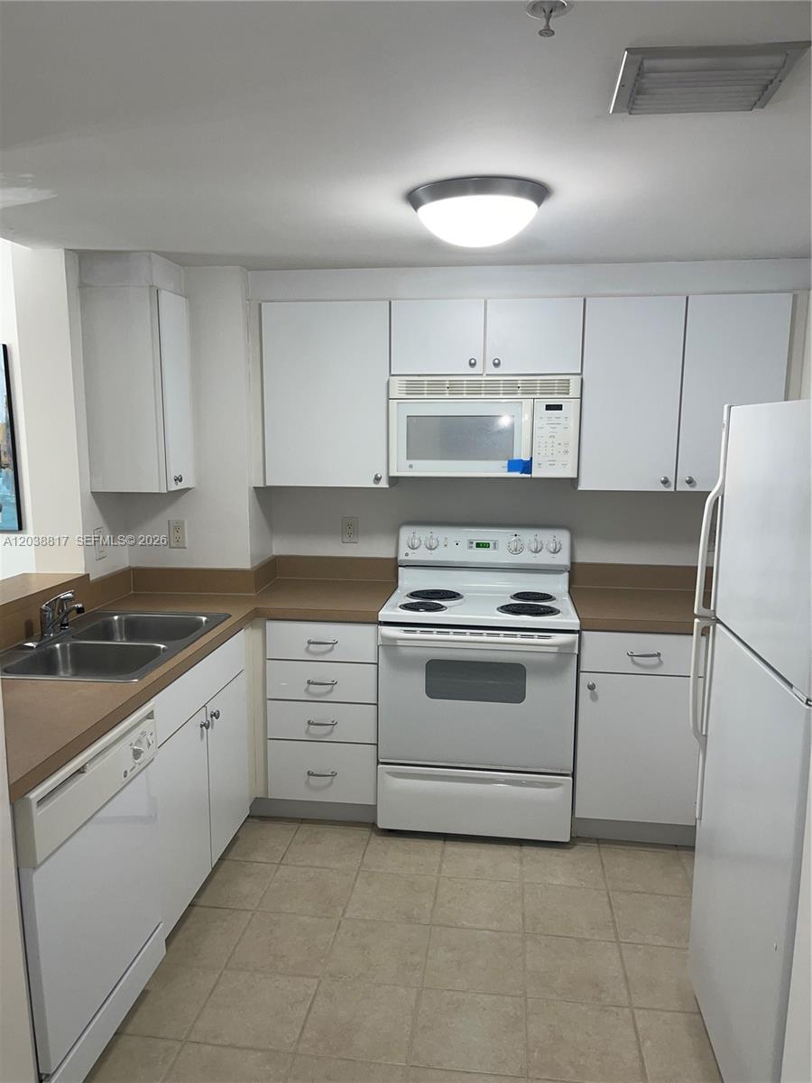 A kitchen features white cabinets, white appliances, and tan countertops with tile flooring — 1250 S Miami Ave # 1410, Miami FL 33130, MIAMI, FL