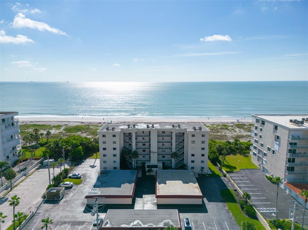 An aerial view shows a multi-story beachfront apartment building with a parking lot and ocean — 299 N ATLANTIC AVENUE UNIT 602, COCOA BEACH, FL