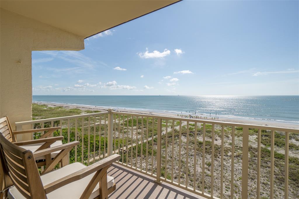 A balcony with two wooden chairs overlooks a sandy beach and the ocean — 299 N ATLANTIC AVENUE UNIT 602, COCOA BEACH, FL