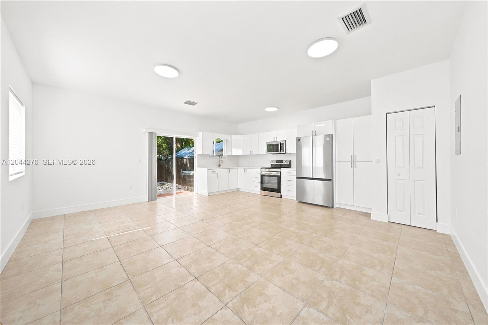 A bright, open-concept kitchen features white cabinetry, stainless steel appliances, and beige tile flooring — 145 NE 60th St # 145, Miami FL 33137, MIAMI, FL