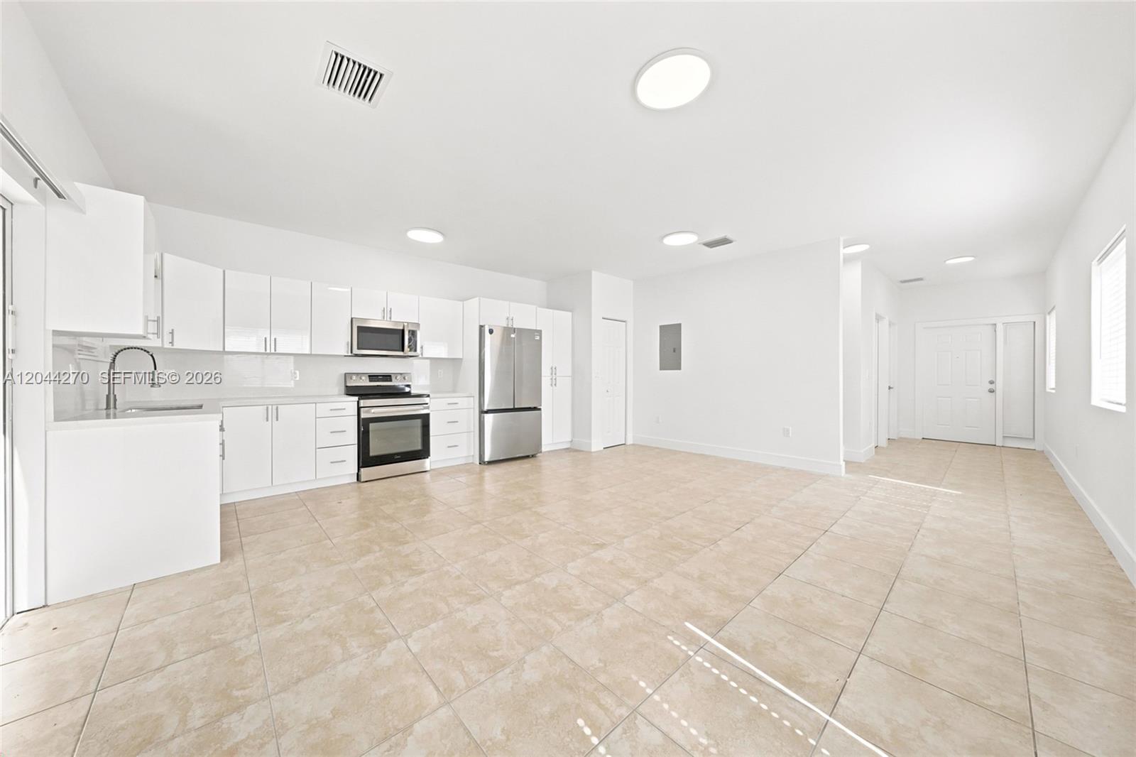 A bright, open-concept kitchen features white cabinetry, stainless steel appliances, and light-colored tile flooring — 145 NE 60th St # 145, Miami FL 33137, MIAMI, FL