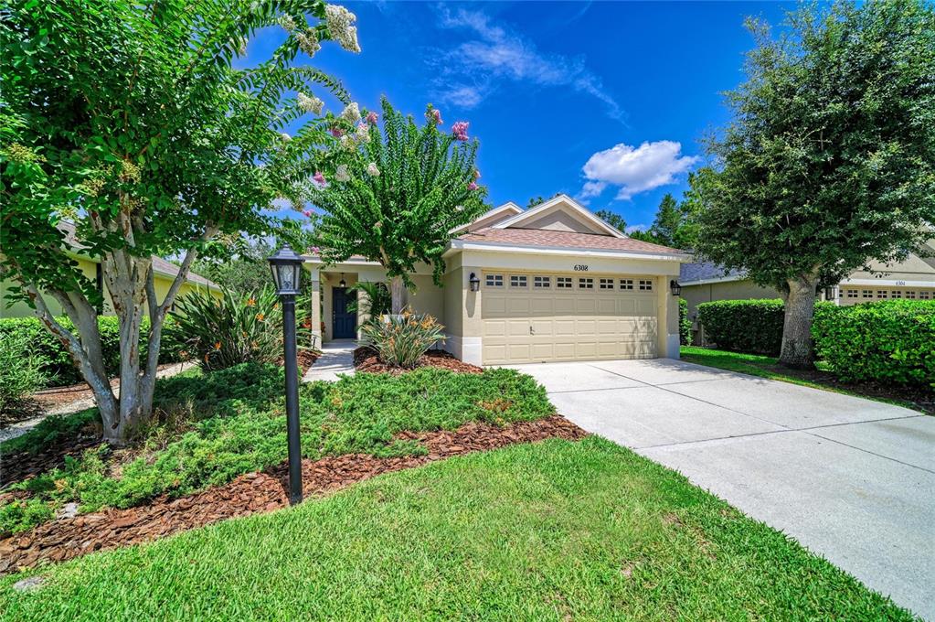 A single-story house with a beige exterior, a two-car garage, and a landscaped front yard — 6308 ROBIN COVE, BRADENTON, FL