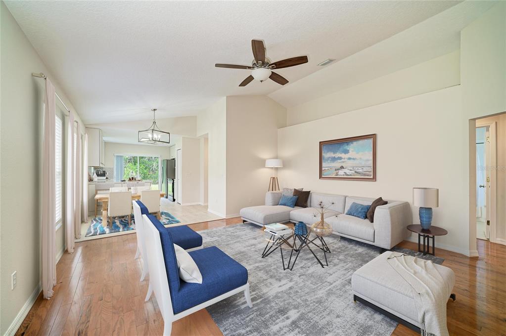 A living room with light hardwood floors, a sectional sofa, and a dining area beyond — 6308 ROBIN COVE, BRADENTON, FL